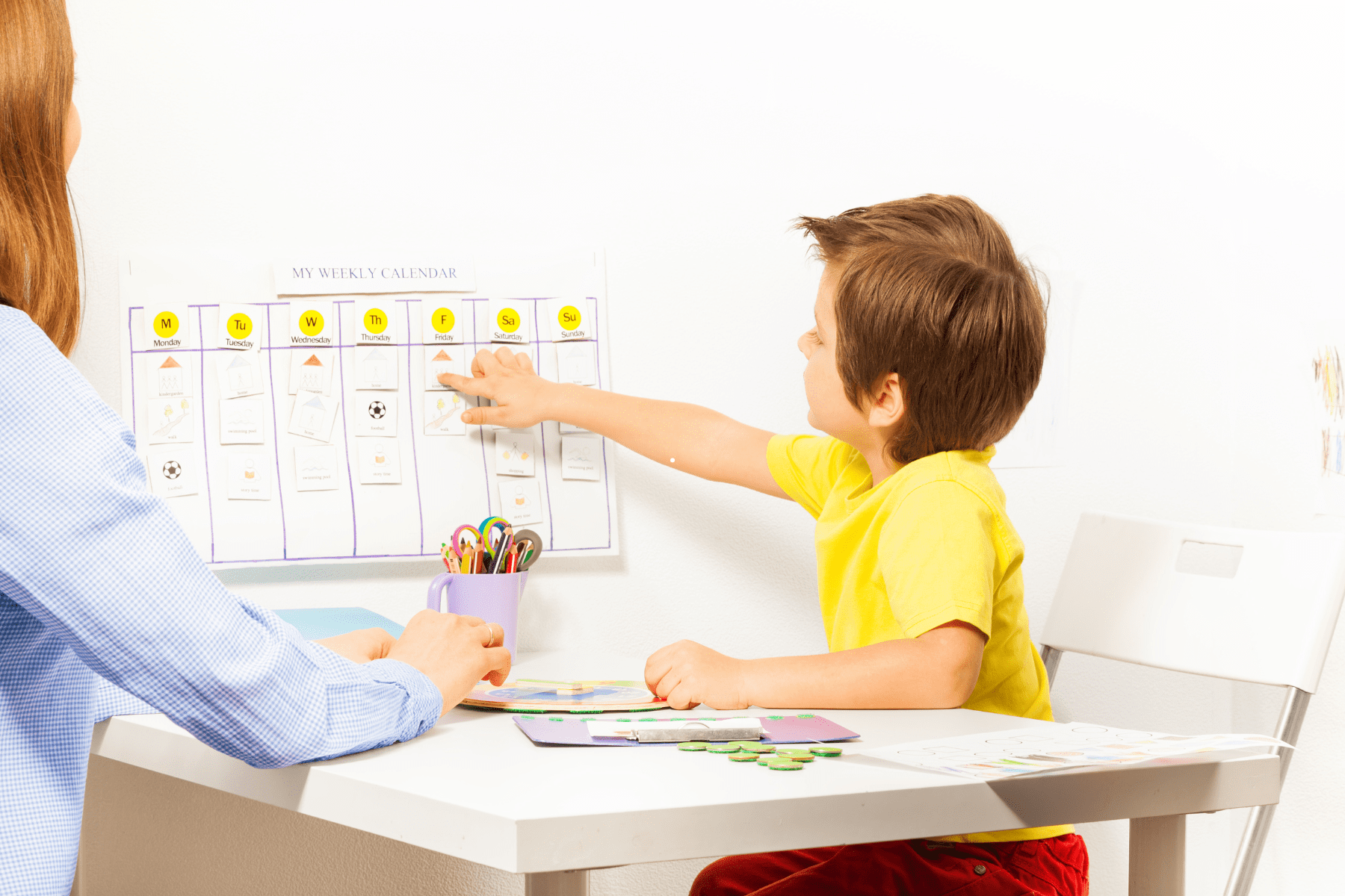 Engaged child pointing at items on a weekly calendar during an ABA therapy session with a supportive therapist.
